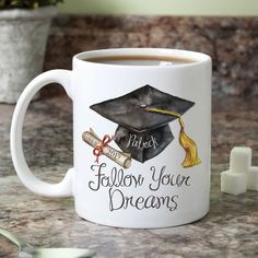 a white coffee mug with a graduation cap and tassel on the side that says, follow your dreams