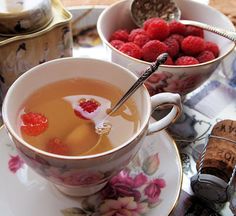 two cups filled with liquid and raspberries on top of a table next to other dishes