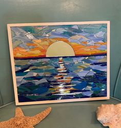 a painting is displayed on a table next to a starfish and seashells