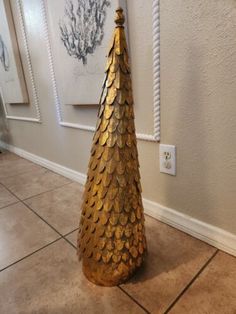 a gold christmas tree is on the floor in front of a white wall and framed pictures