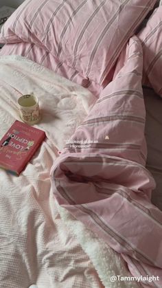 a bed with pink comforter and pillows on top of it next to a book