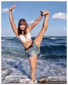 a woman standing on one leg in the water with her arms up and legs spread out