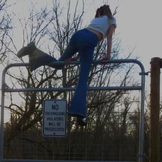 a woman standing on top of a metal fence next to a forest with no trespassing