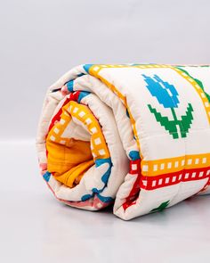 a white blanket with multicolored designs on it sitting on a table next to an orange object