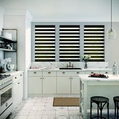 a kitchen with marble counter tops and white cabinets, along with black shuttered windows