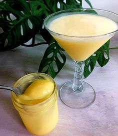 a glass filled with yellow liquid next to a potted plant and a spoon in it