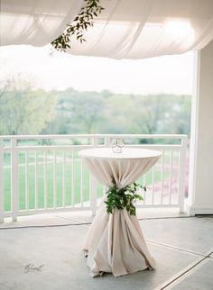 the table is set up on the porch for an outdoor wedding ceremony with white drapes and greenery