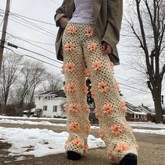 a woman wearing crocheted pants with flowers on the bottom and legs, standing in front of snow covered ground