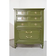 a green chest of drawers with gold handles and knobs on each drawer, against a white wall