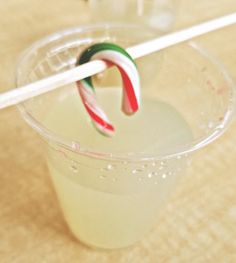 two candy canes sticking out of a drink in a plastic cup on a table