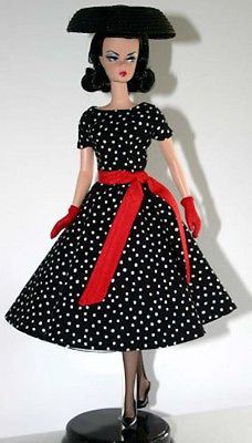 a black and white polka dot dress with red ribbon around the waist is worn by a doll