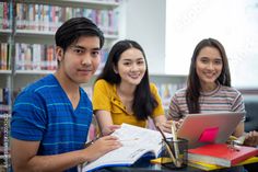 three young people sitting at a table with books and laptops in front of them