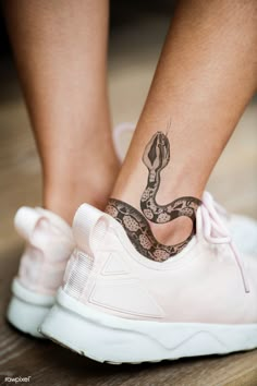 a woman's foot with a snake tattoo on her left ankle and white sneakers