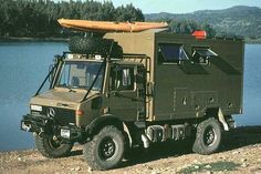 an army truck with a kayak strapped to the roof is parked near a body of water