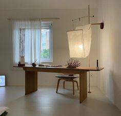 a room with a table, chair and lamp on it in front of a window