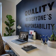 there is a desk with a laptop on it in front of a wall that says quality is everyone's responsability