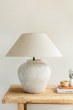 a white lamp sitting on top of a wooden table next to a book and vase