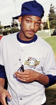 a baseball player holding a cell phone in his right hand and wearing a blue hat