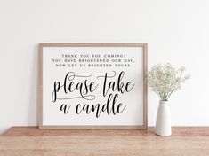 a white vase sitting on top of a wooden table next to a sign that says please take a candle