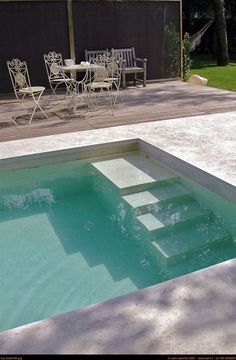 an empty swimming pool in the middle of a backyard with chairs and tables around it