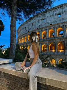 a beautiful young woman sitting on top of a stone wall next to an ancient building