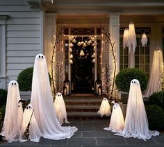 a group of ghost statues in front of a house decorated with white lights and decorations