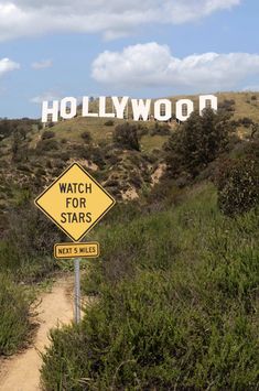 a yellow sign that says watch for stars on the side of a hill next to bushes