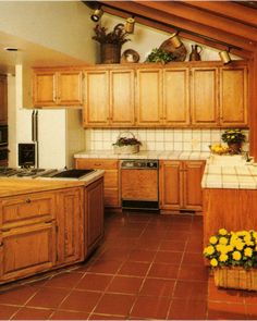 a kitchen with wooden cabinets and tile flooring is shown in this image, there are yellow flowers on the counter