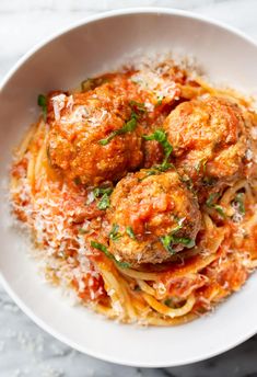 spaghetti and meatballs with tomato sauce in a white bowl on a marble table top