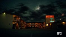 the motel is lit up at night with clouds in the sky and lights shining on the building