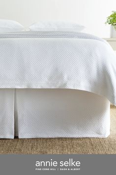 a bed with white sheets and pillows on top of carpeted floor next to potted plant