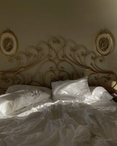 an unmade bed with white sheets and gold headboard