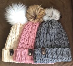 three beanies with pom - poms on top of each other, sitting on a couch