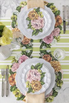 the table is set with plates, silverware and yellow flowers on green striped napkins