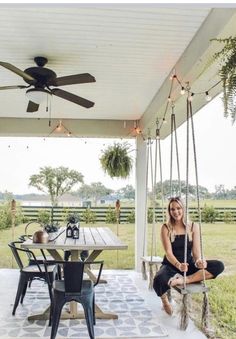 a woman sitting on a porch swing in front of a table with chairs and a ceiling fan