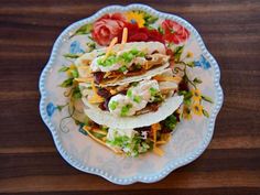 a plate topped with three tacos covered in cheese and toppings on top of a wooden table