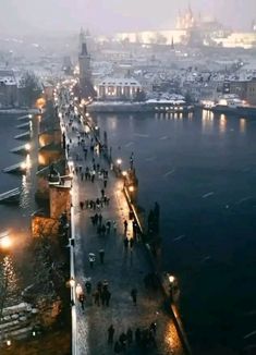 people are walking on the side of a bridge at night in winter, with snow covering the ground and buildings behind them