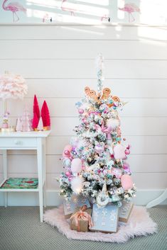 a pink and white christmas tree with presents under it in a room that has flamingos on the walls