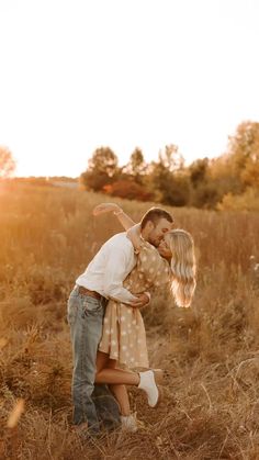 a man and woman kissing in the middle of an open field with tall brown grass