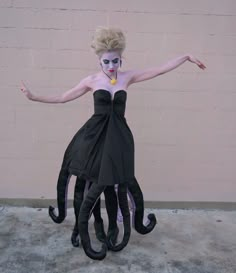 a woman dressed up as an octopus with makeup on her face and hands, standing in front of a brick wall