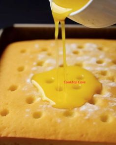 someone pouring yellow sauce on top of a cake in a pan with holes around the edges