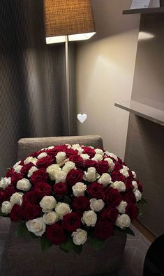 a large bouquet of red and white roses in a room with a lamp on the wall