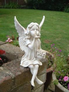 a statue of an angel sitting on top of a brick wall next to some flowers