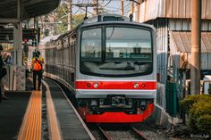 a red and silver train pulling into a station with people standing on the platform next to it