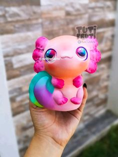 a hand holding a small toy that looks like a pink and blue animal with big eyes