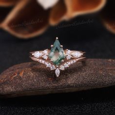 a green and white diamond ring sitting on top of a piece of wood next to a flower