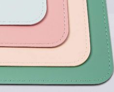 three pastel colored coasters with white stitching on each side and one has a green, pink, and blue rectangle