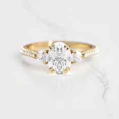 an oval cut diamond ring with three small diamonds on the band, set in 18k yellow gold