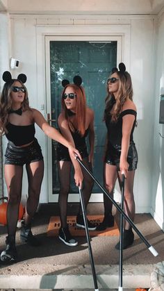 three women dressed up as mickey mouses in front of a door with brooms