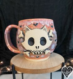 a ceramic cat mug sitting on top of a wooden chair with two holes in it